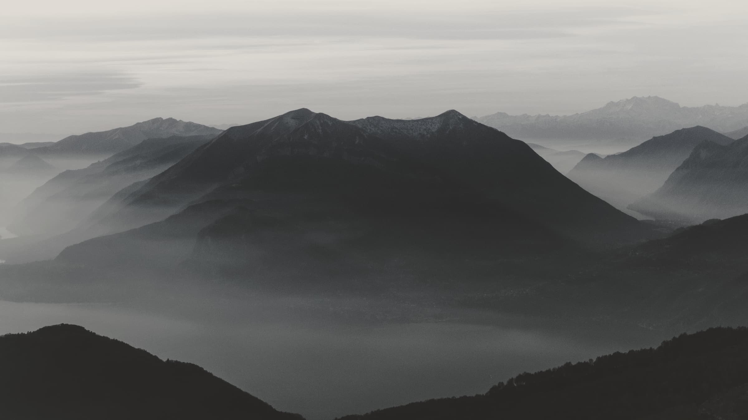 Layered mountain ridges at first light, a pale sky above and mist lying in the valley at their feet.