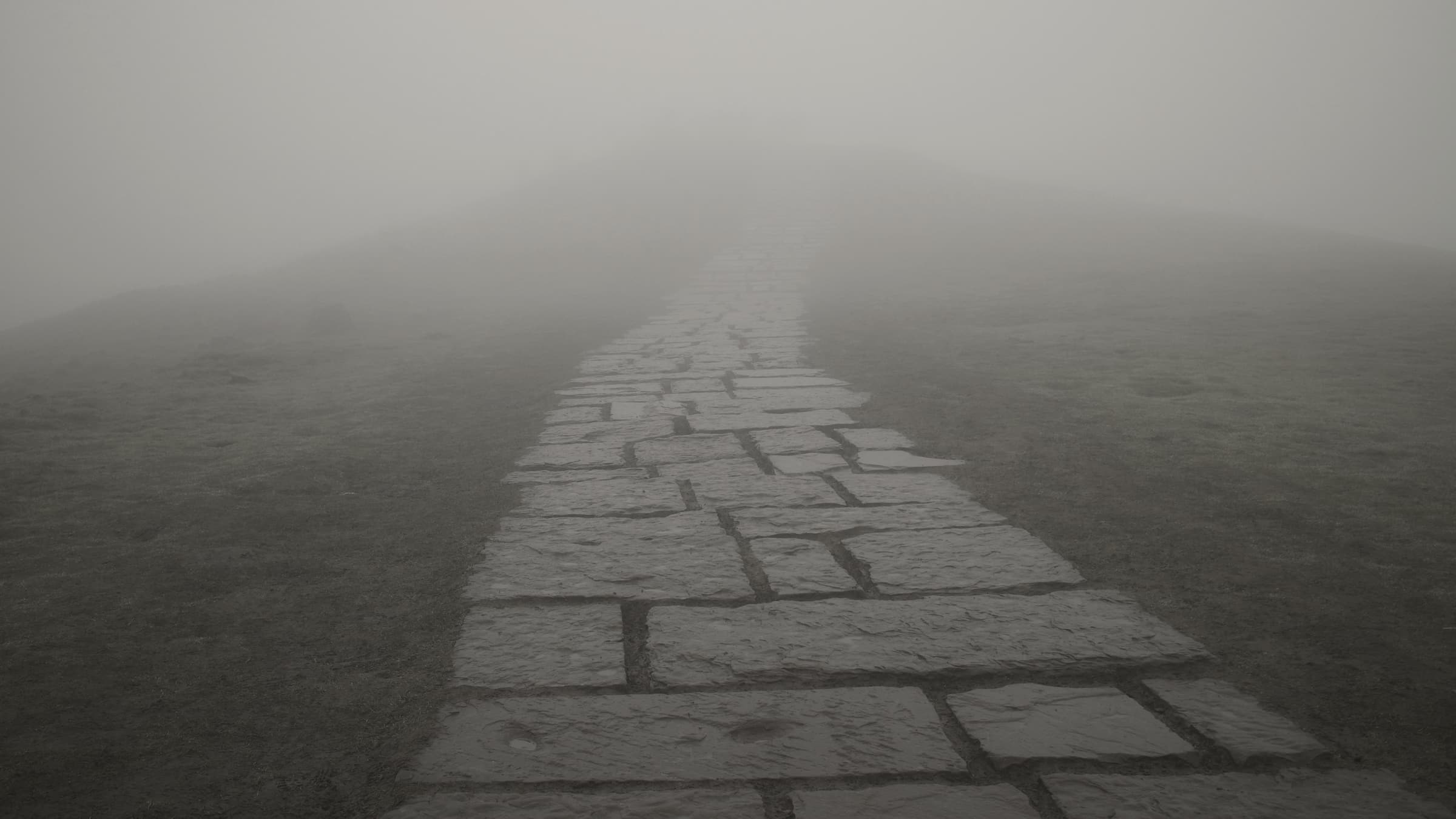 A path of worn stone slabs leading uphill and disappearing into thick fog.